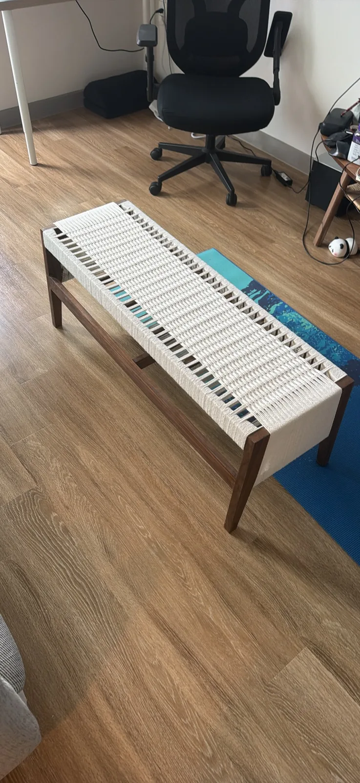 The finished bench seen from standing height at an angle, showing the full length of the woven seat, the splayed legs and the lower stretcher between them