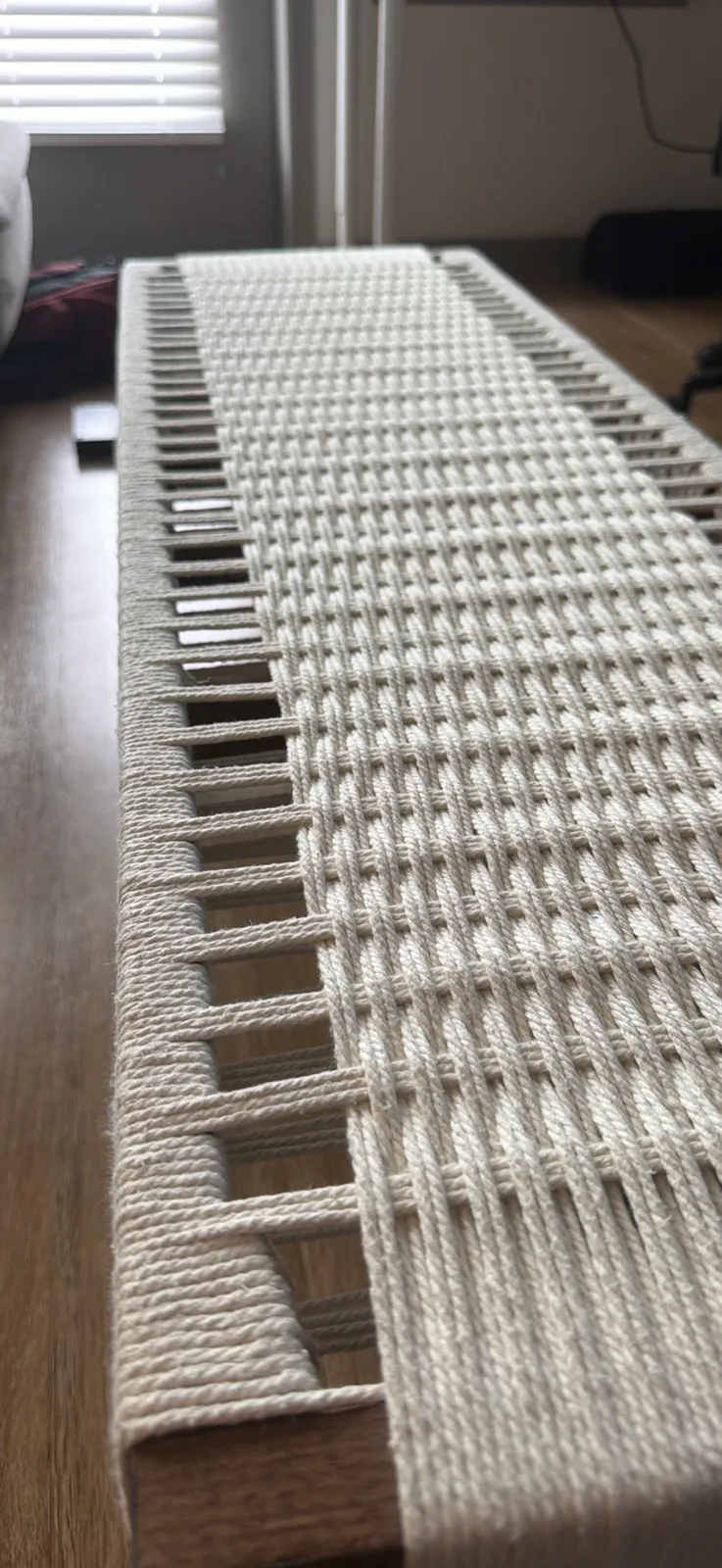 Macro photograph of the woven seat, showing individual cords wrapping over the wooden rail on the left and interlacing into a diagonal twill pattern to the right