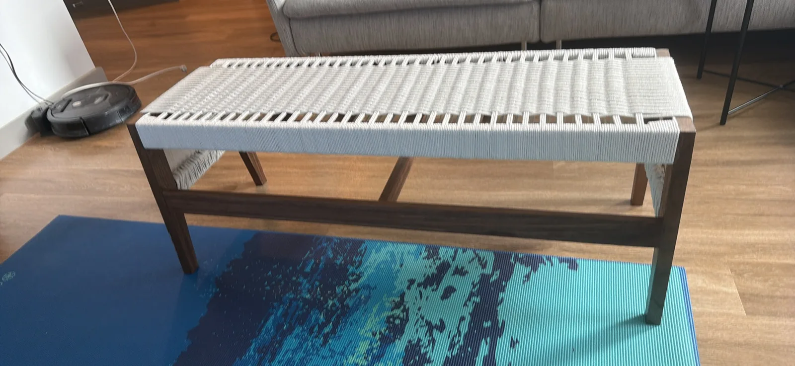 The bench photographed square from the side at a low angle, so the seat rails, the four splayed legs and the full length lower stretcher all read as one structure