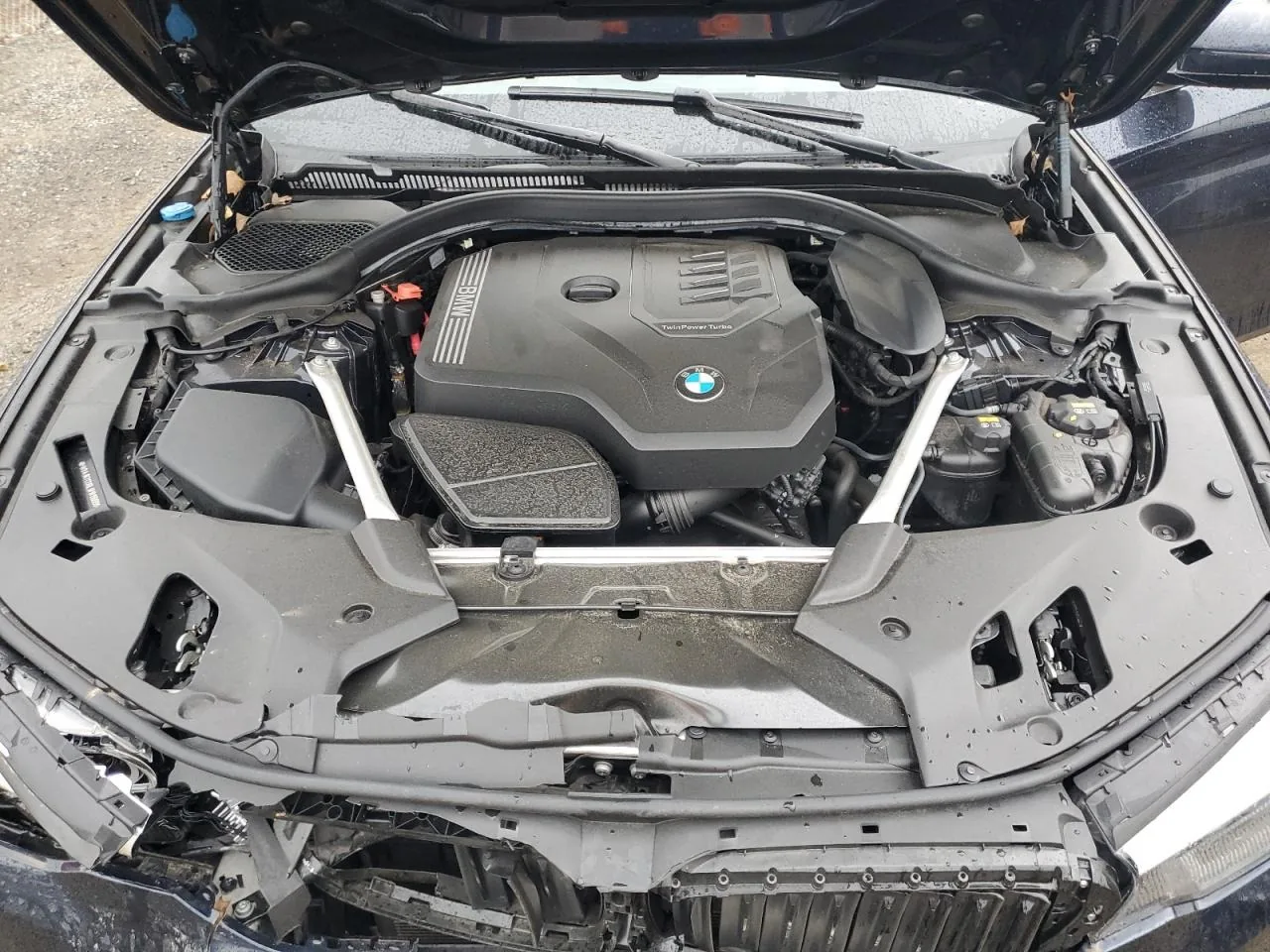 An open engine bay with a four cylinder engine under a black cover, and the panel across the front of the bay bent and crumpled