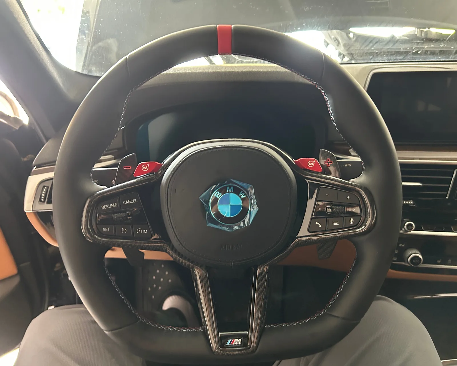 A black steering wheel with a red stripe at 12 o'clock, carbon fibre spokes, red M1 and M2 buttons and an M badge on the lower spoke