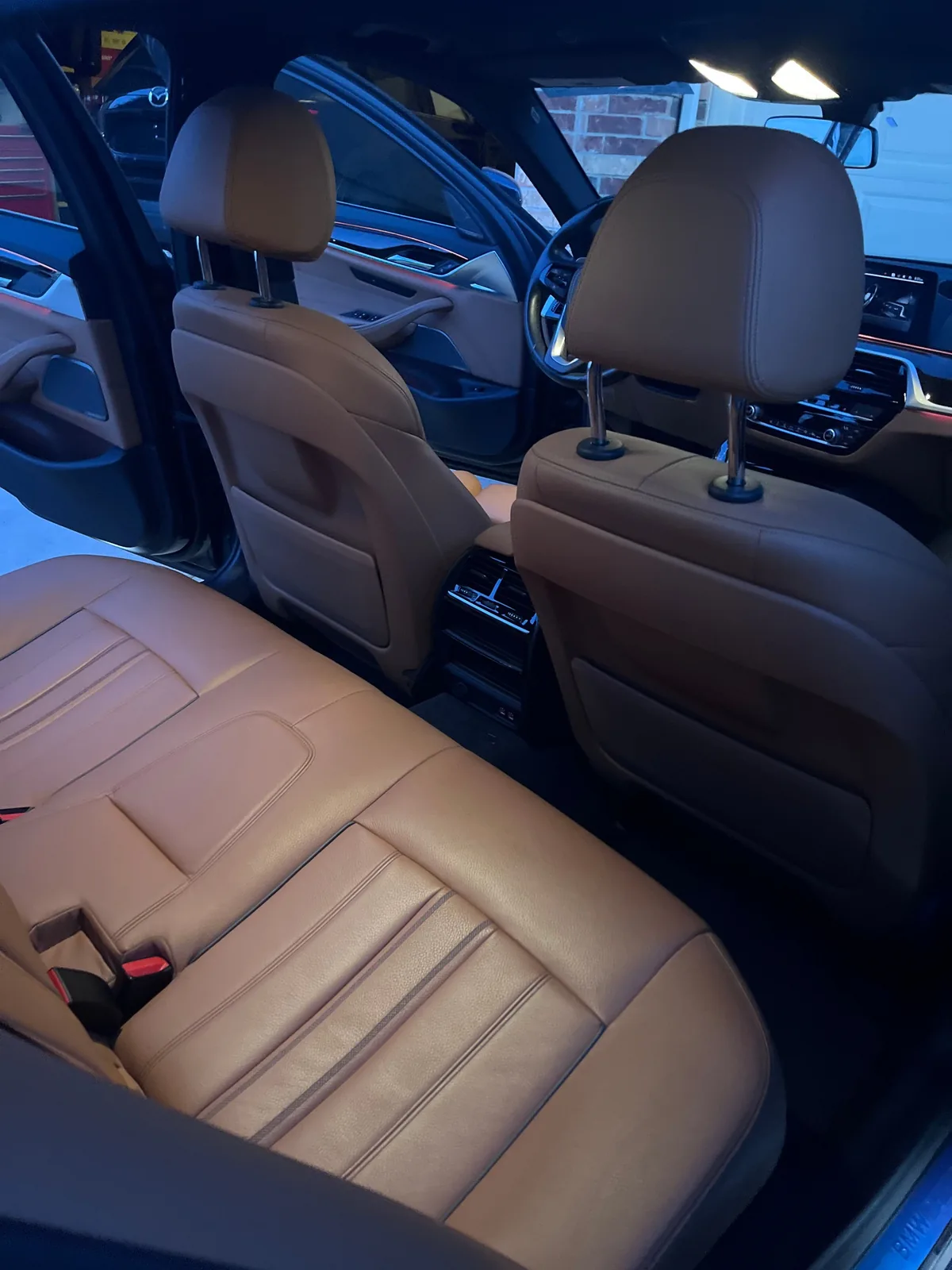 The cognac leather back seat and the backs of the two front seats, seen through an open rear door, with the dashboard lit up ahead