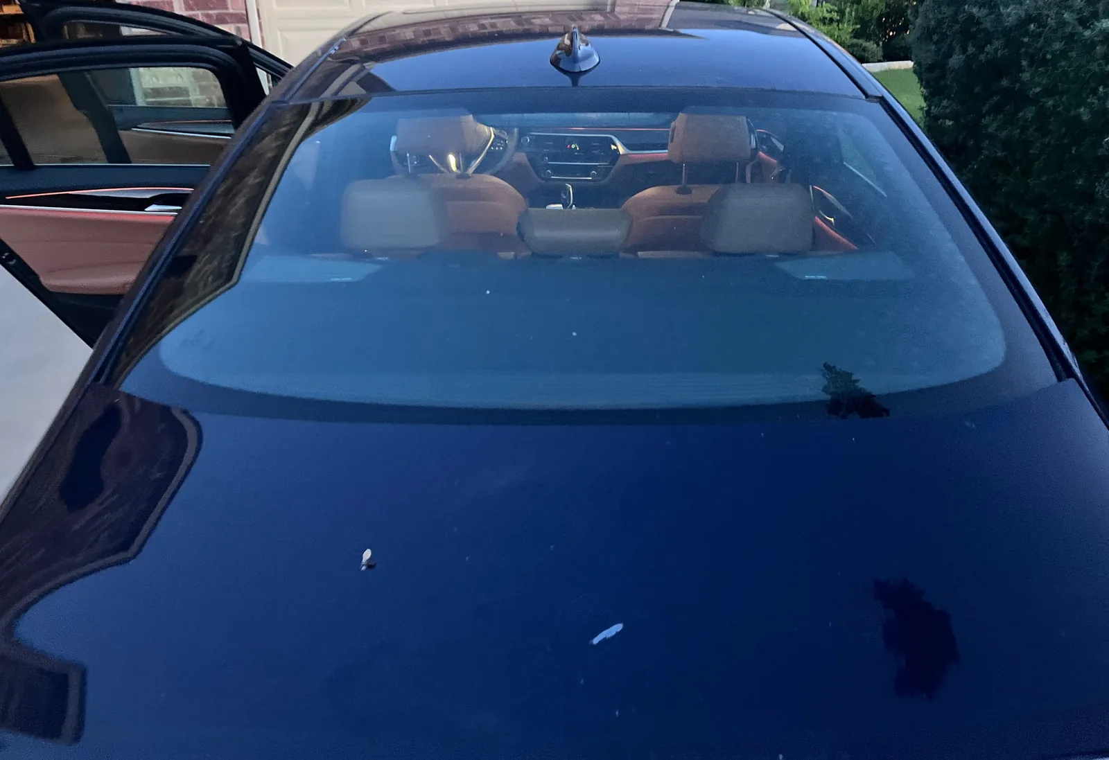 Looking along the dark blue trunk lid to the rear window, with the cognac headrests and the lit dashboard inside and a rear door open on the left