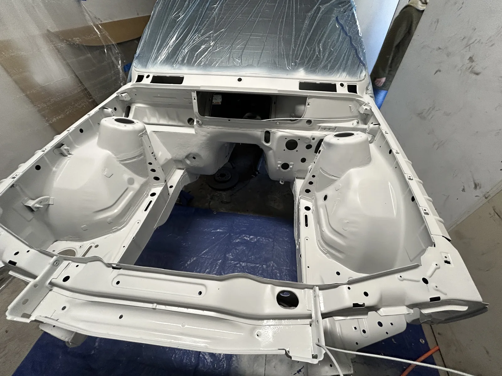 The E30 engine bay stripped to bare metal and sprayed in light grey primer, seen from the front with the windscreen masked off