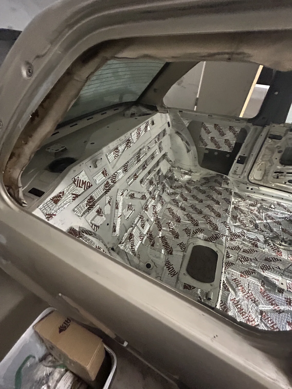 Looking through the door opening into the stripped interior of the E30, the floor and wheel arches covered in foil backed sound deadening mat