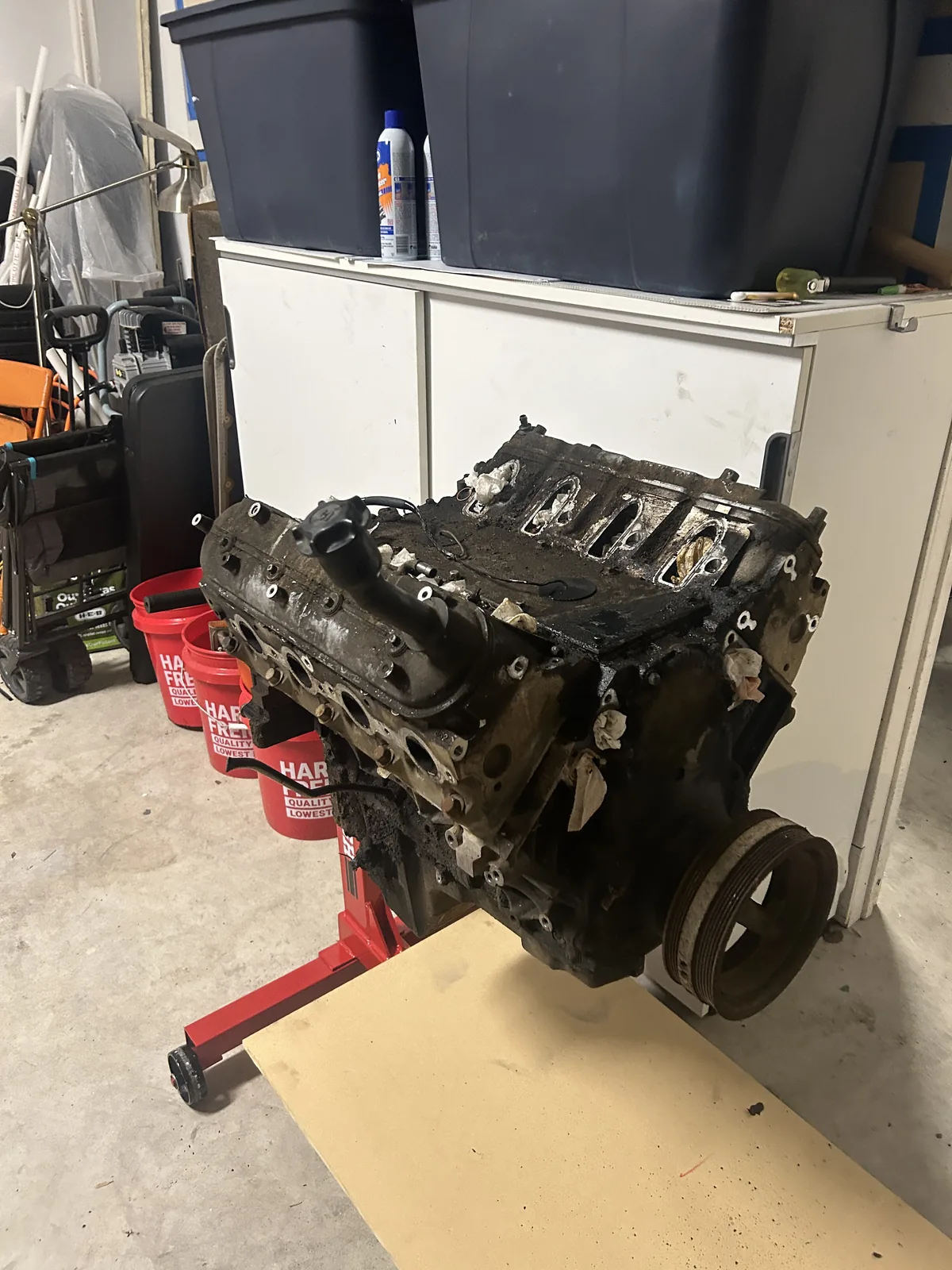 The four cylinder engine removed from the car and mounted on a red engine stand in a garage, dirty and partly disassembled