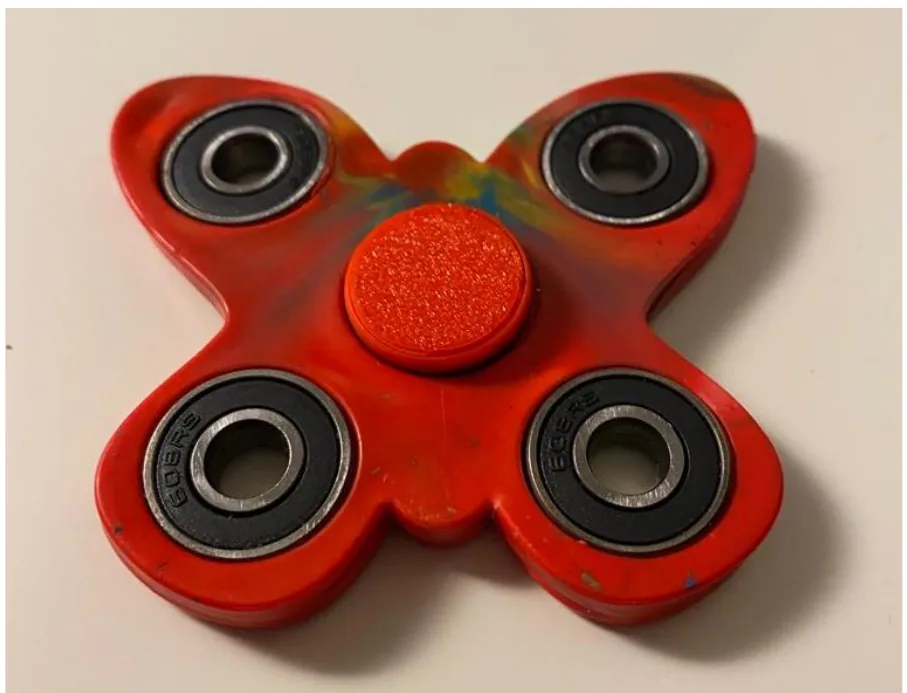 A four armed fidget spinner in marbled red, blue and yellow plastic with four steel ball bearings and a red printed cap at the centre