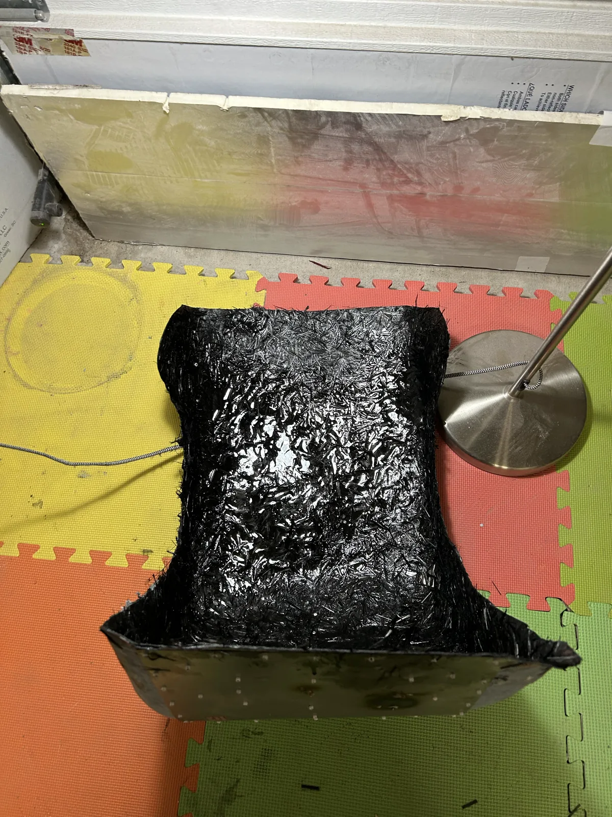 A black forged carbon racing seat shell standing upright, its surface marbled with chopped fiber