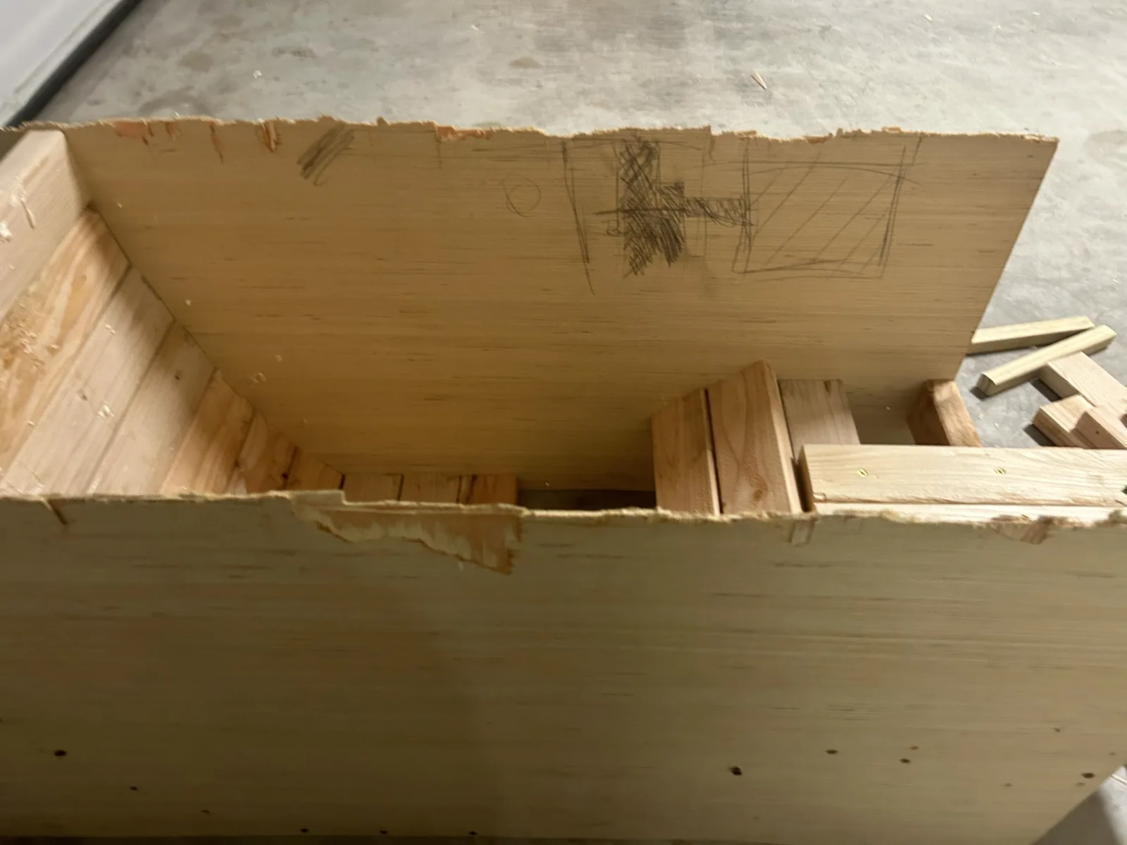 An open plywood box on trestles with a curved seat profile sketched in pencil on its back wall