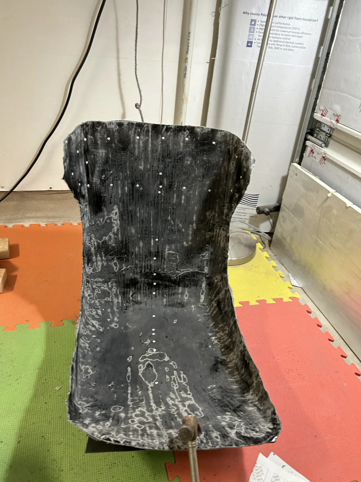 A rough black carbon seat shell just removed from its mold, white release residue on the surface