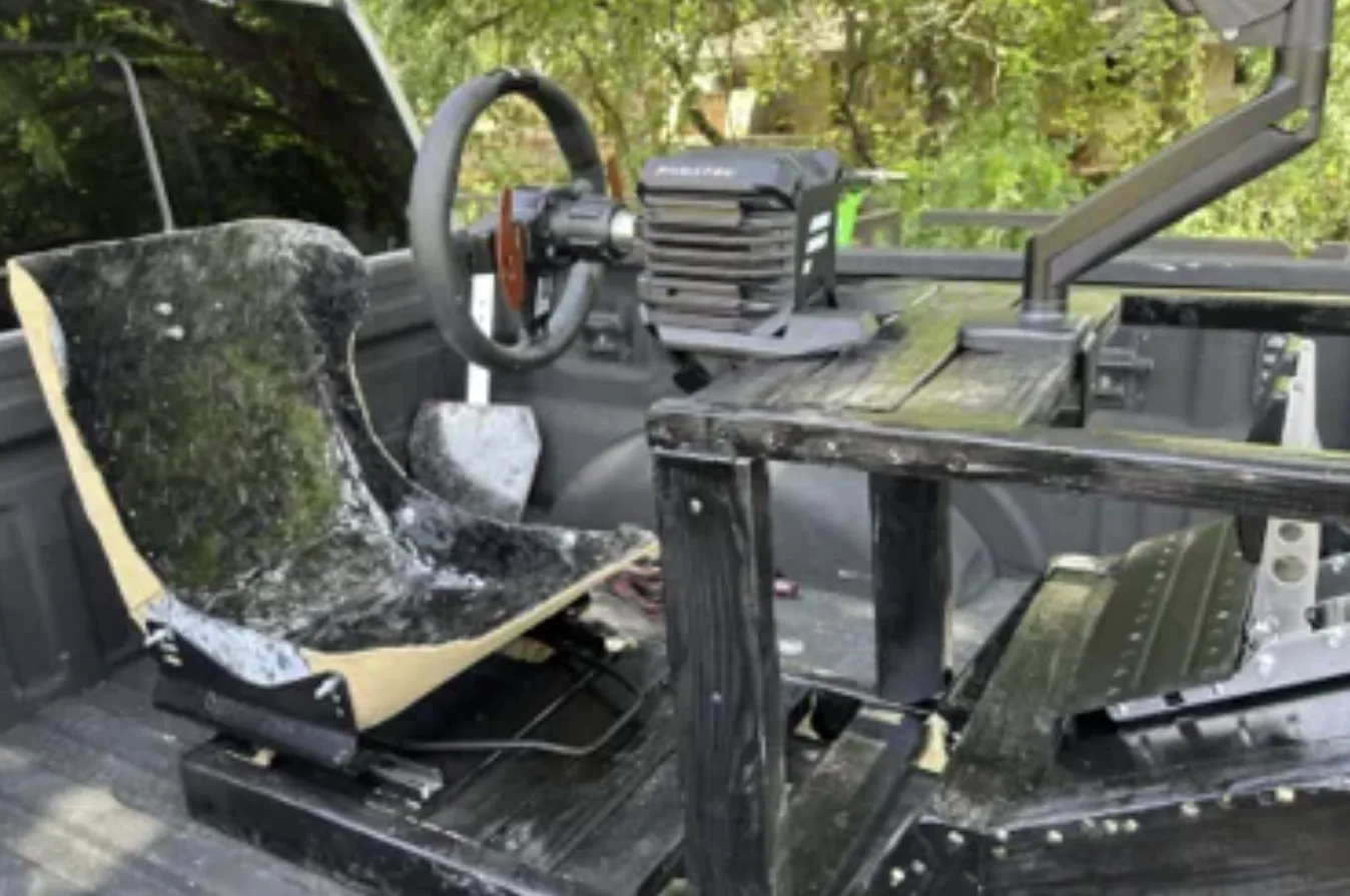 The assembled simulator rig with carbon seat, steering wheel, pedals and monitor arm sitting in a pickup bed