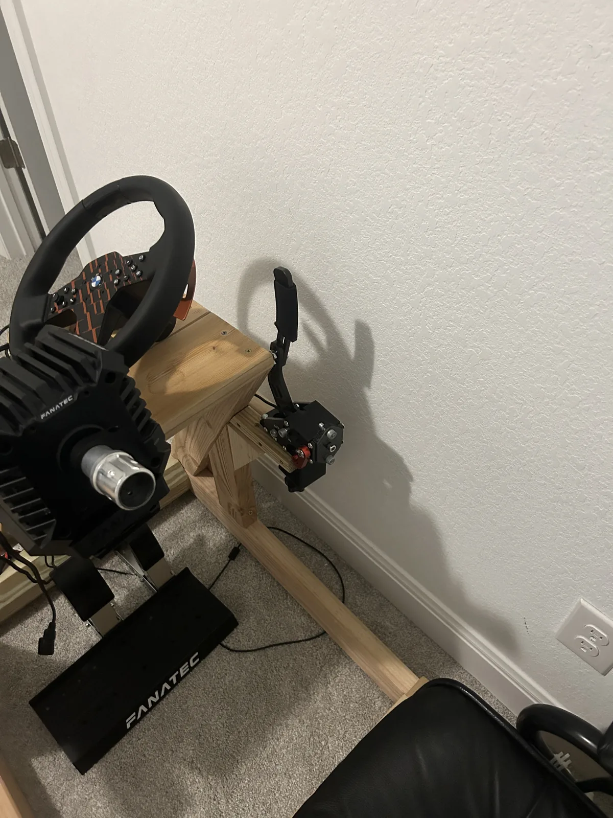 The sim rig seen along its length from behind the wheel, showing the seat, the wheel base and the pedal plate all on one timber frame