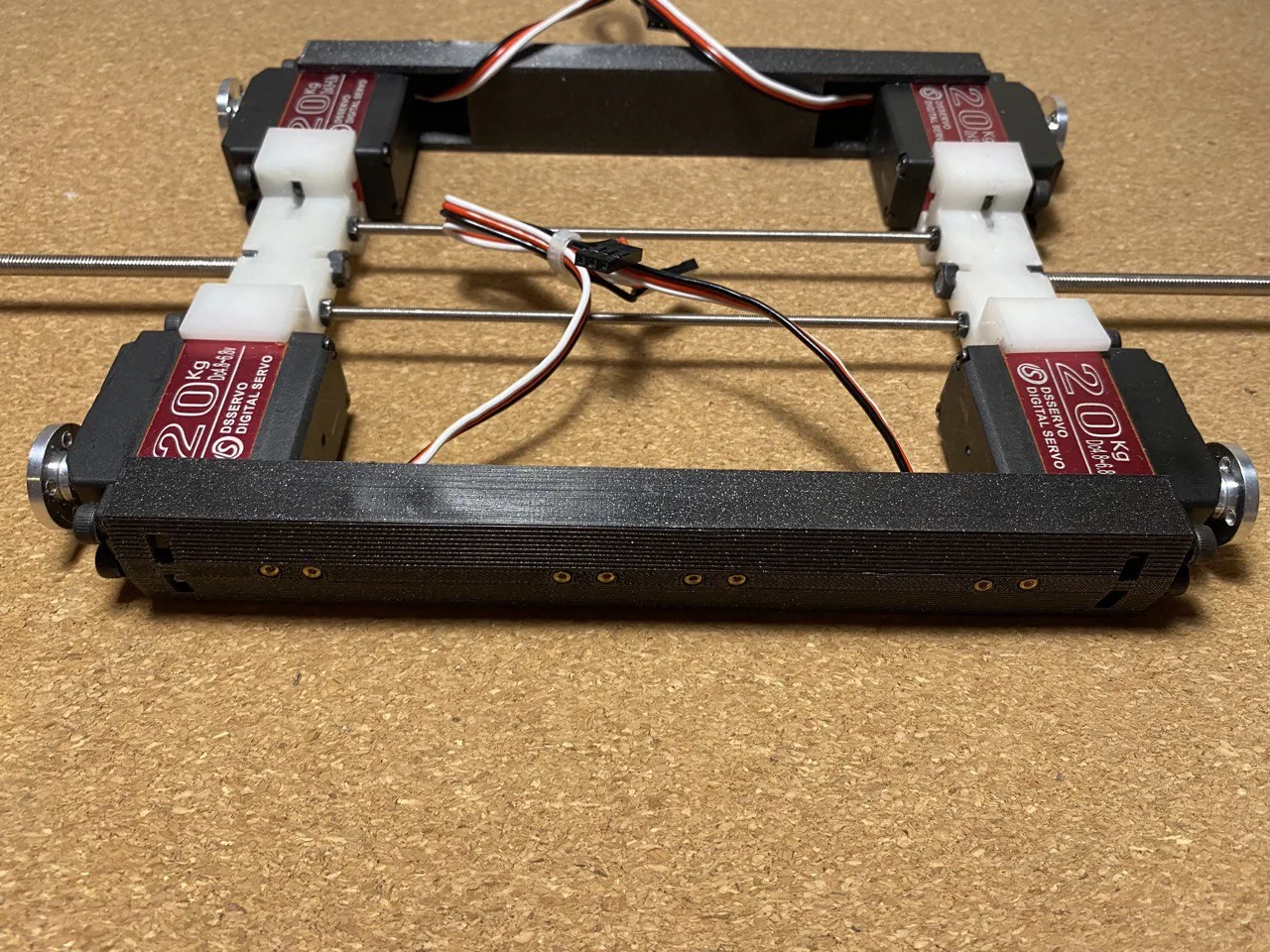 A bare rectangular robot chassis with four servos mounted and two steel rods running its length