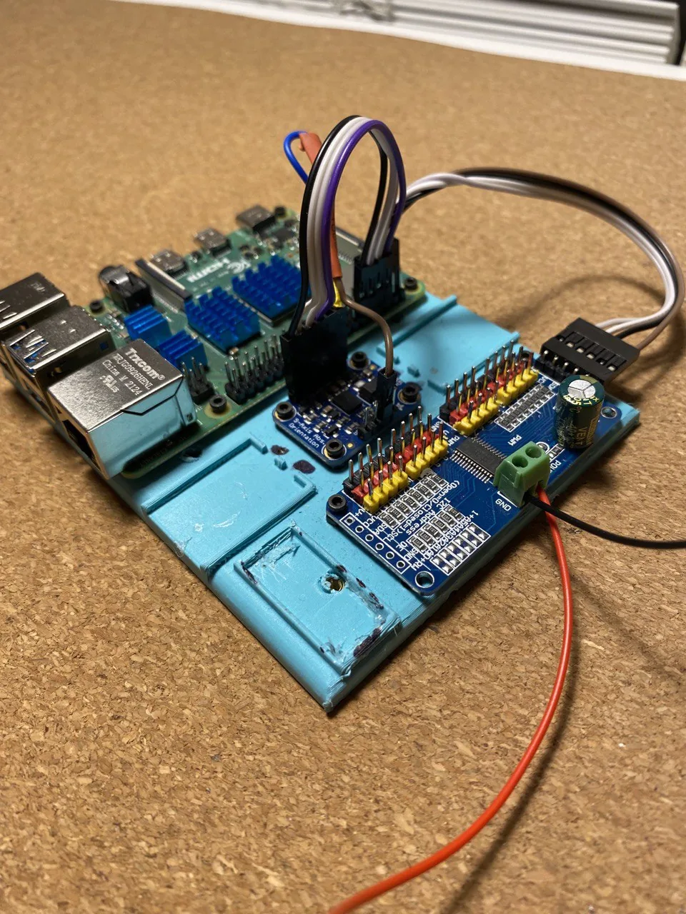 A Raspberry Pi stacked with a blue servo driver board, jumper wires and a power lead attached