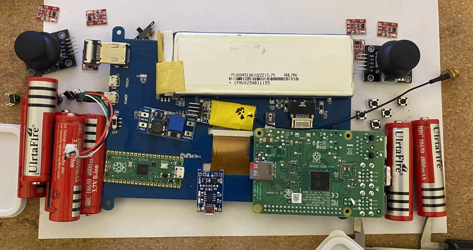 An open handheld controller board with two joysticks, a microcontroller and four cylindrical batteries