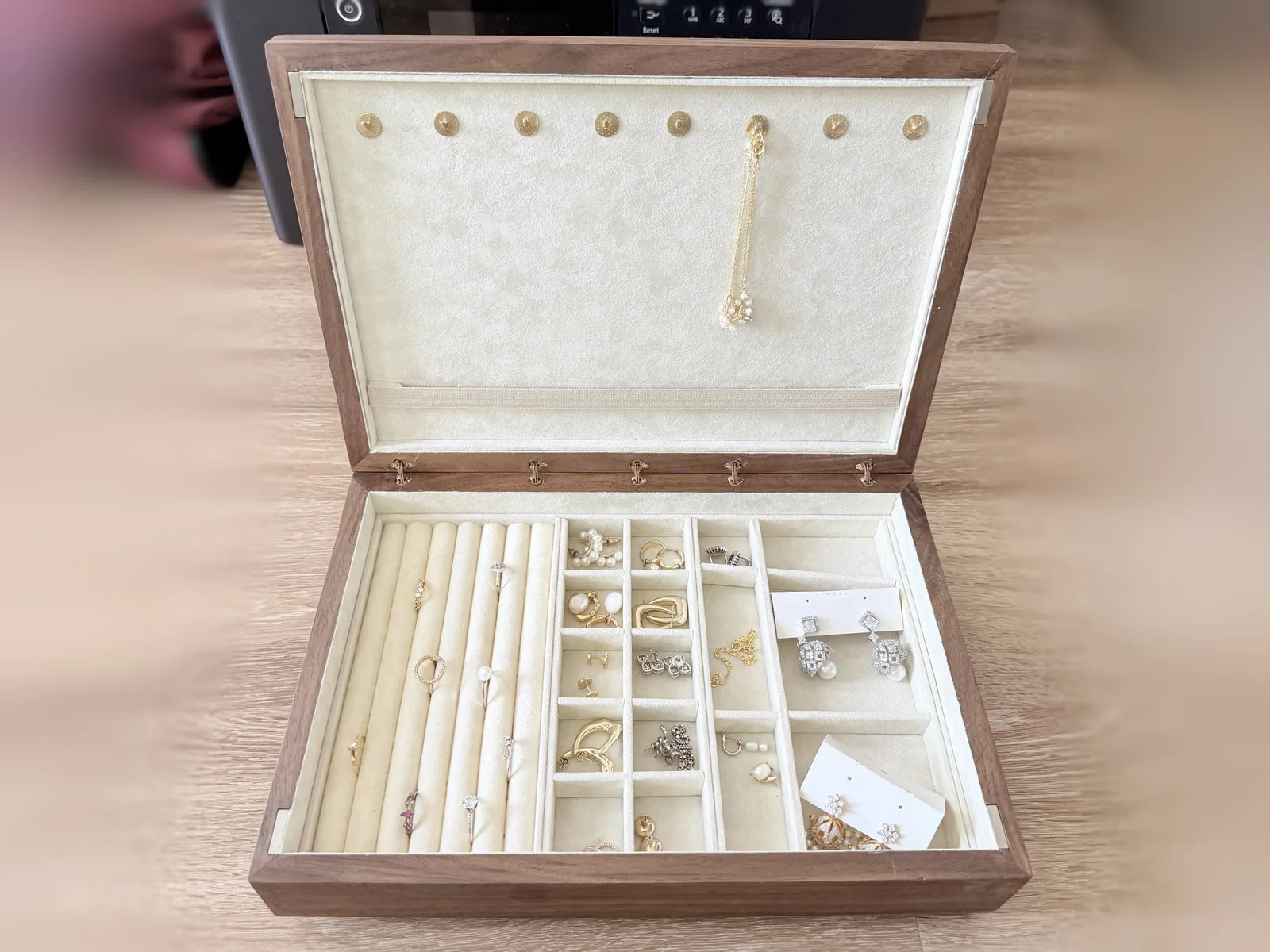 The open jewelry box with a fine gold chain hanging from one of the brass hooks in the lid, the loaded tray visible in the base beneath it