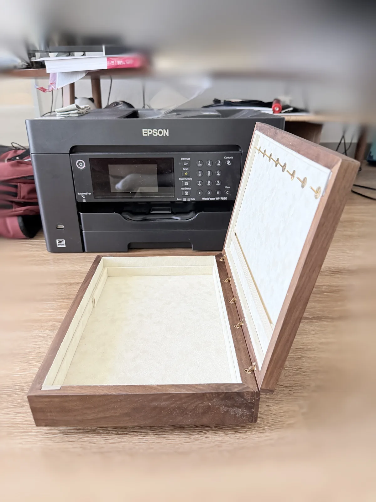 The jewelry box open and standing on a desk, seen from the front, its lid folded back past vertical, with a blurred office desk behind