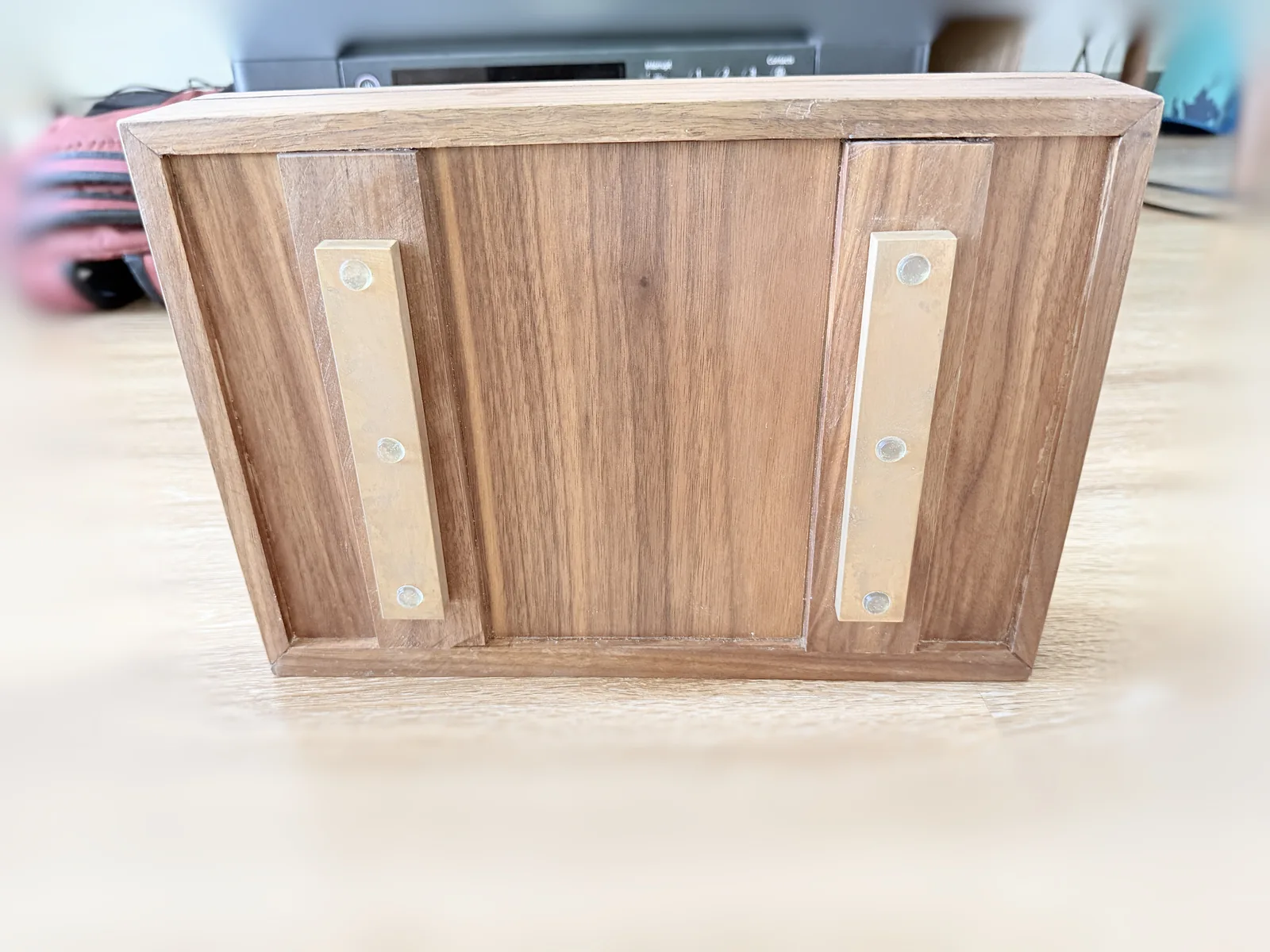 The jewelry box stood upright showing its back face, a framed panel in dark hardwood with two vertical brass plates each fixed by three screws