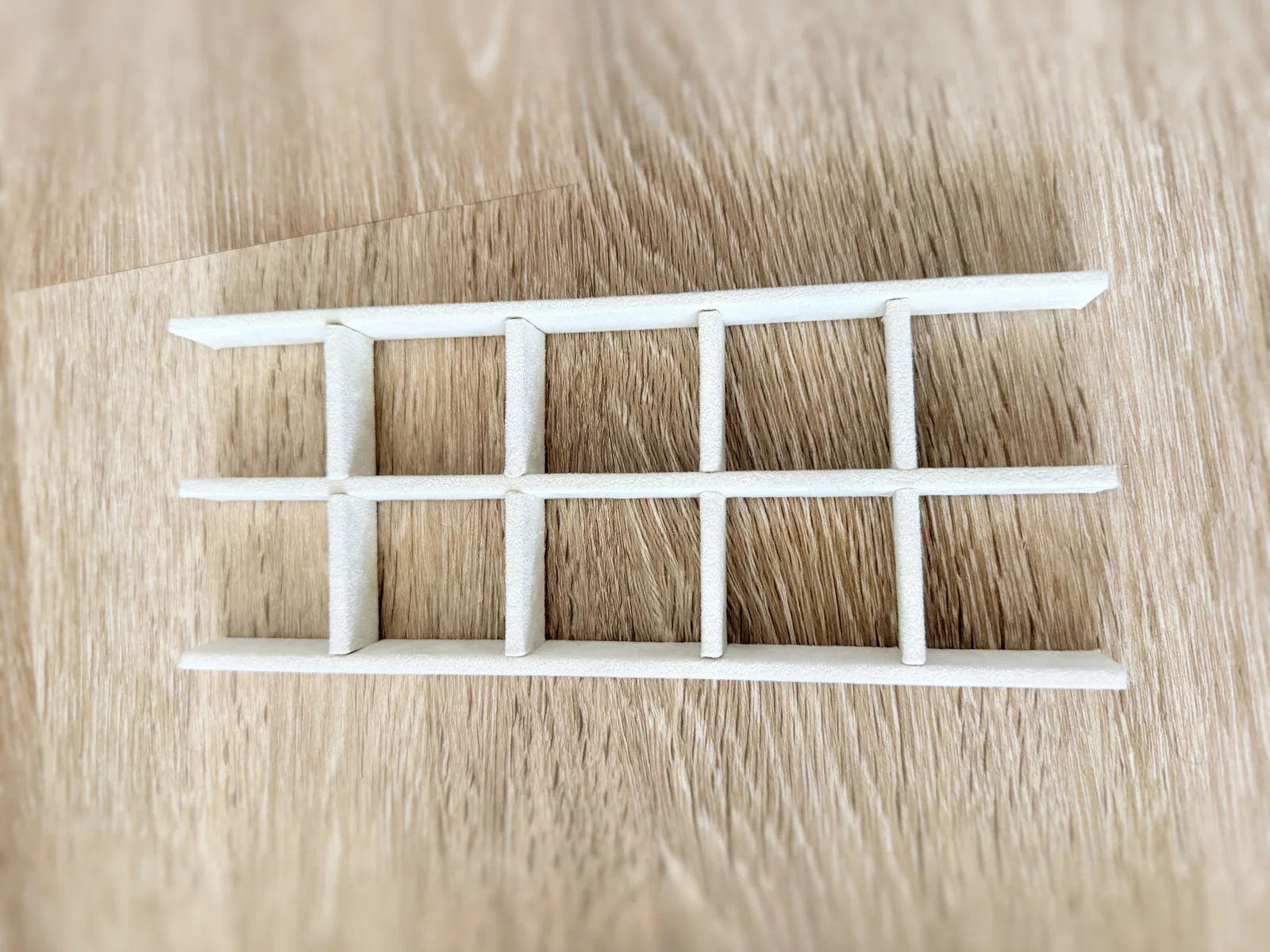 A cream coloured lattice of thin strips laid flat on a wood floor, forming a grid of rectangular compartments, the strips notched into one another where they cross
