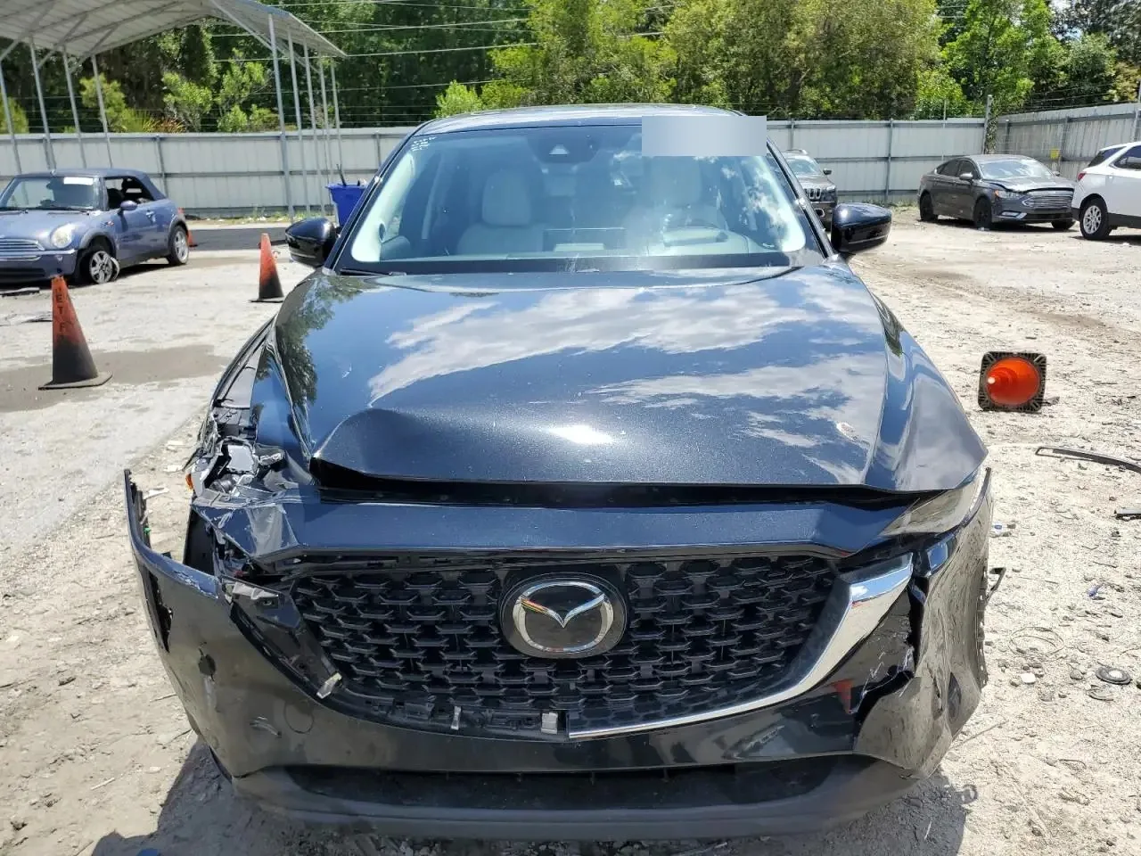 The front of the damaged CX-5 seen head on, with the hood creased along its front edge, the grille still in place and the bumper torn and hanging at both corners