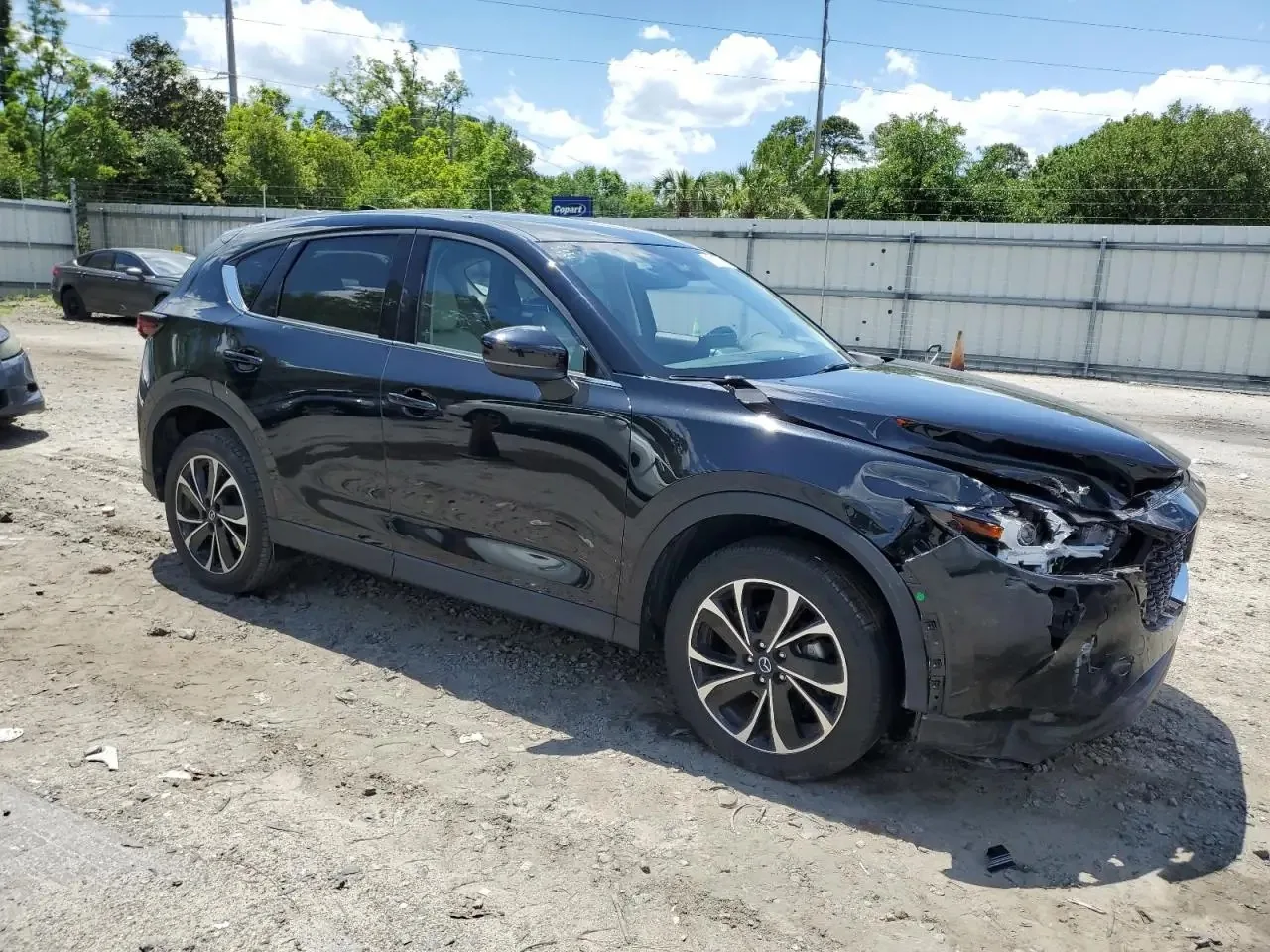 The damaged CX-5 seen from the front right, with the headlight broken open, the bumper cover crushed and torn, and the hood crumpled at that corner