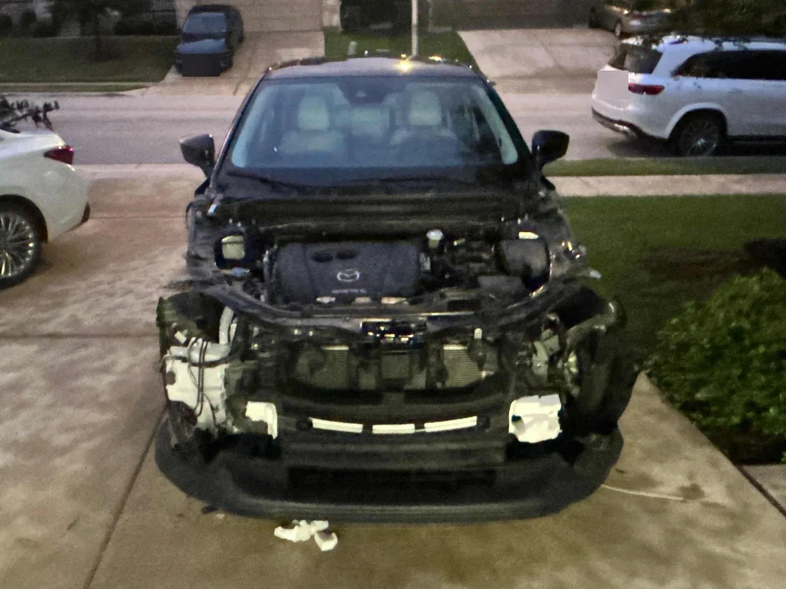 The CX-5 at dusk seen head on with the whole front end removed, showing the engine cover, the radiator and the bare structure behind the bumper