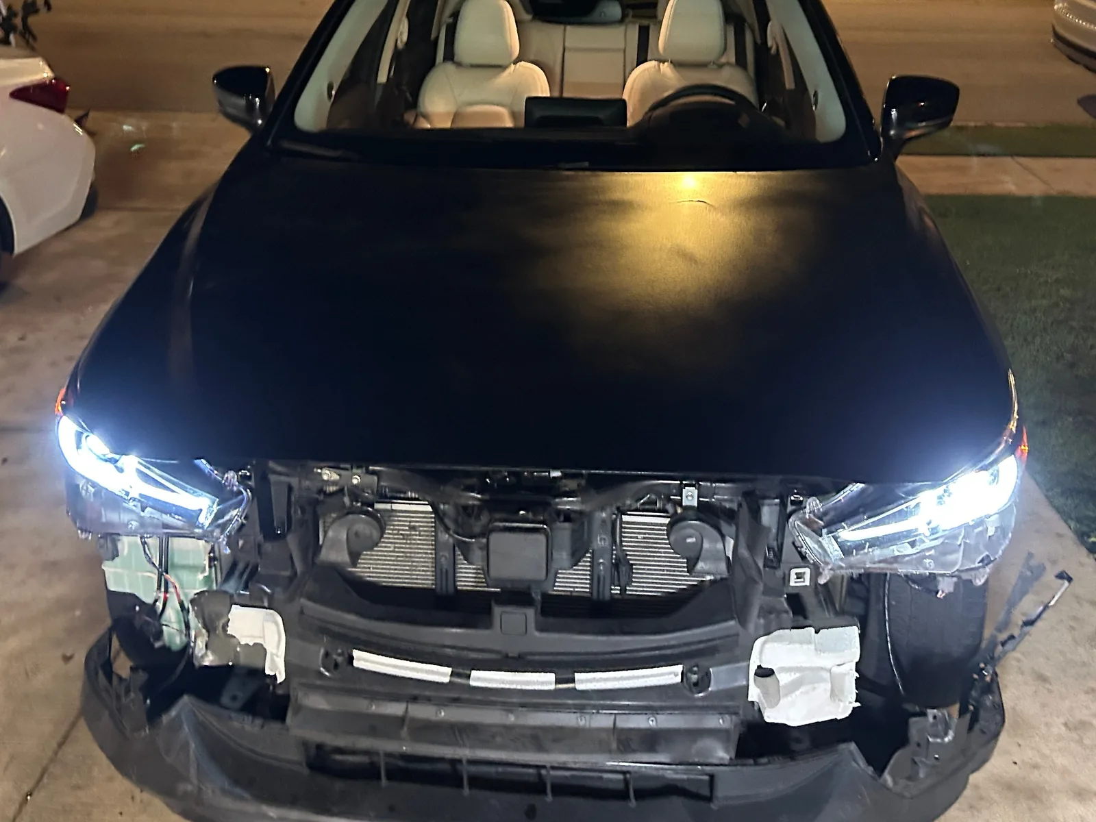 The CX-5 at night seen head on with a dull black hood fitted and both headlights lit, and the radiator and lower bumper still exposed below them