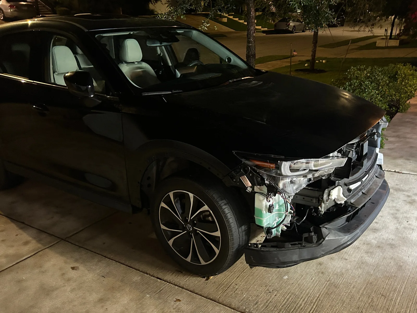 The CX-5 at night from the front right, with the headlight fitted, the washer fluid tank and wiring showing, and only the lower bumper left at the front