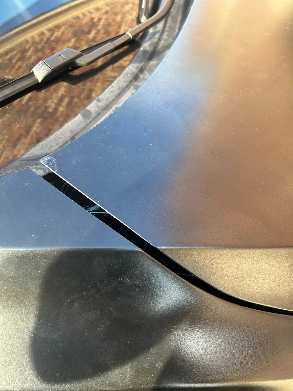 A close-up of the corner where the hood meets the fender near the windshield, with a wide, dark gap running between the two dull panels