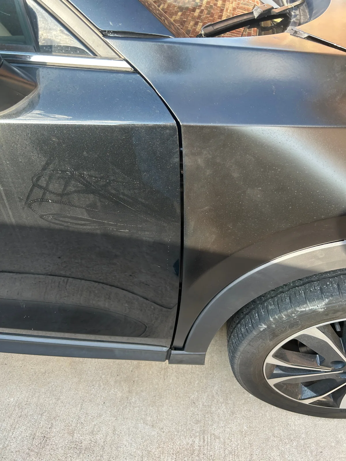 A close-up of the seam between the fender and the front door, with dust on both panels and the front wheel at the bottom right