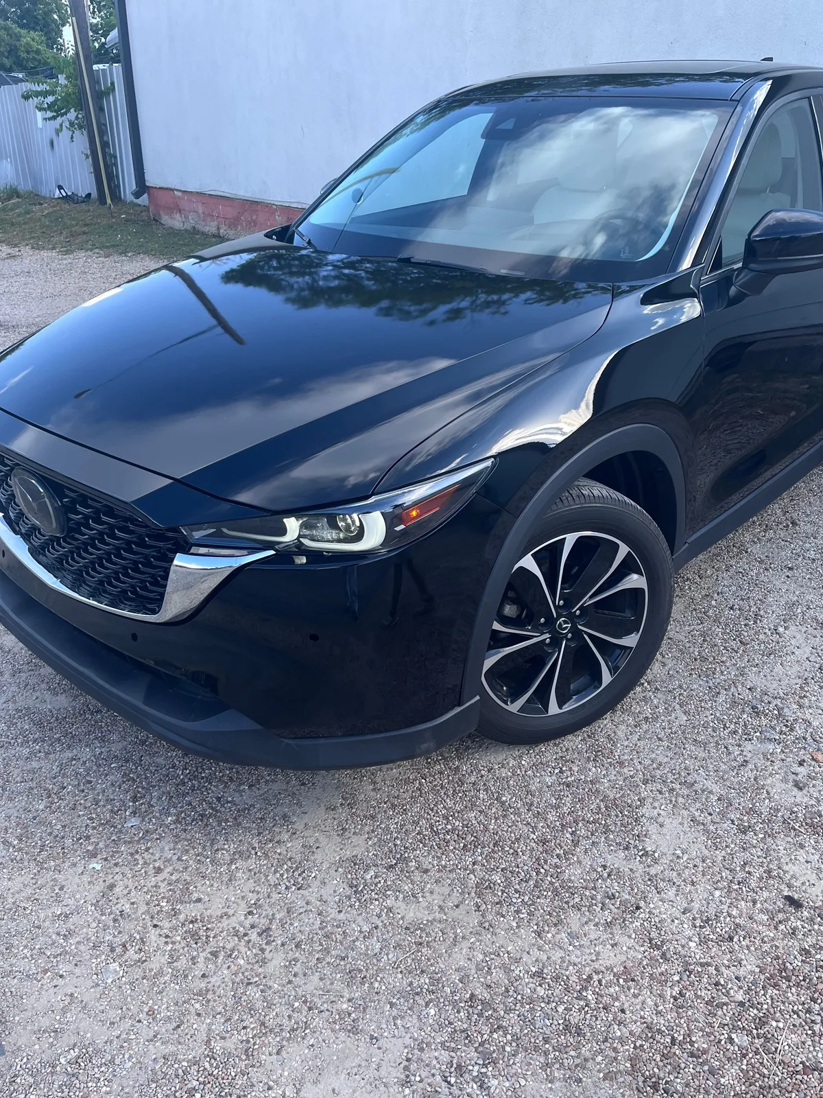 The finished CX-5 from the front left, glossy black with the grille and headlight in, parked on gravel