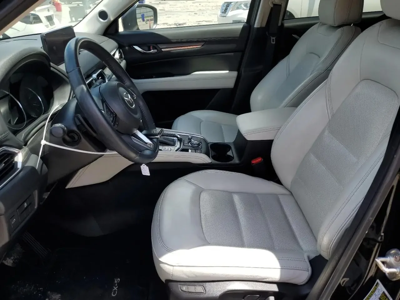 The CX-5's light grey leather front seats seen through the open driver's door, with the steering wheel and the gear selector