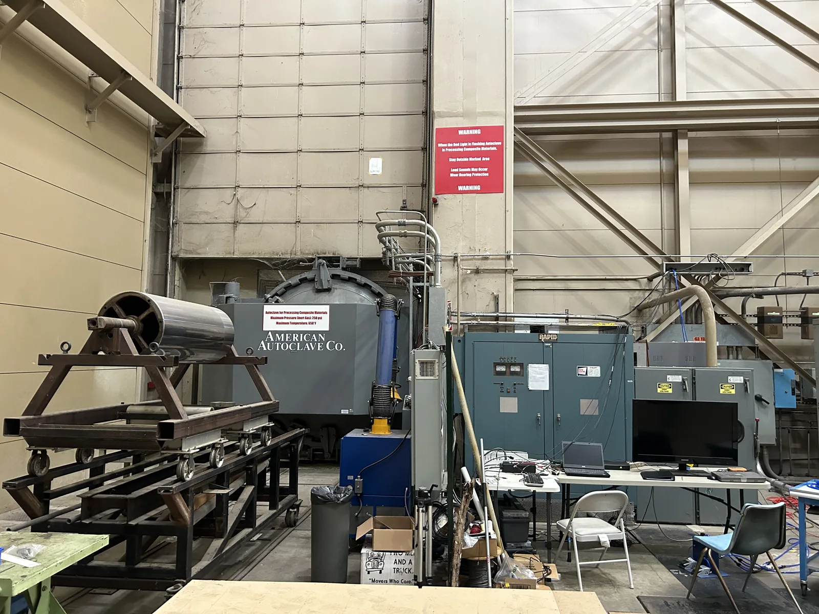 An industrial autoclave marked American Autoclave Co. in a university high-bay laboratory, alongside steel test frames and workbenches