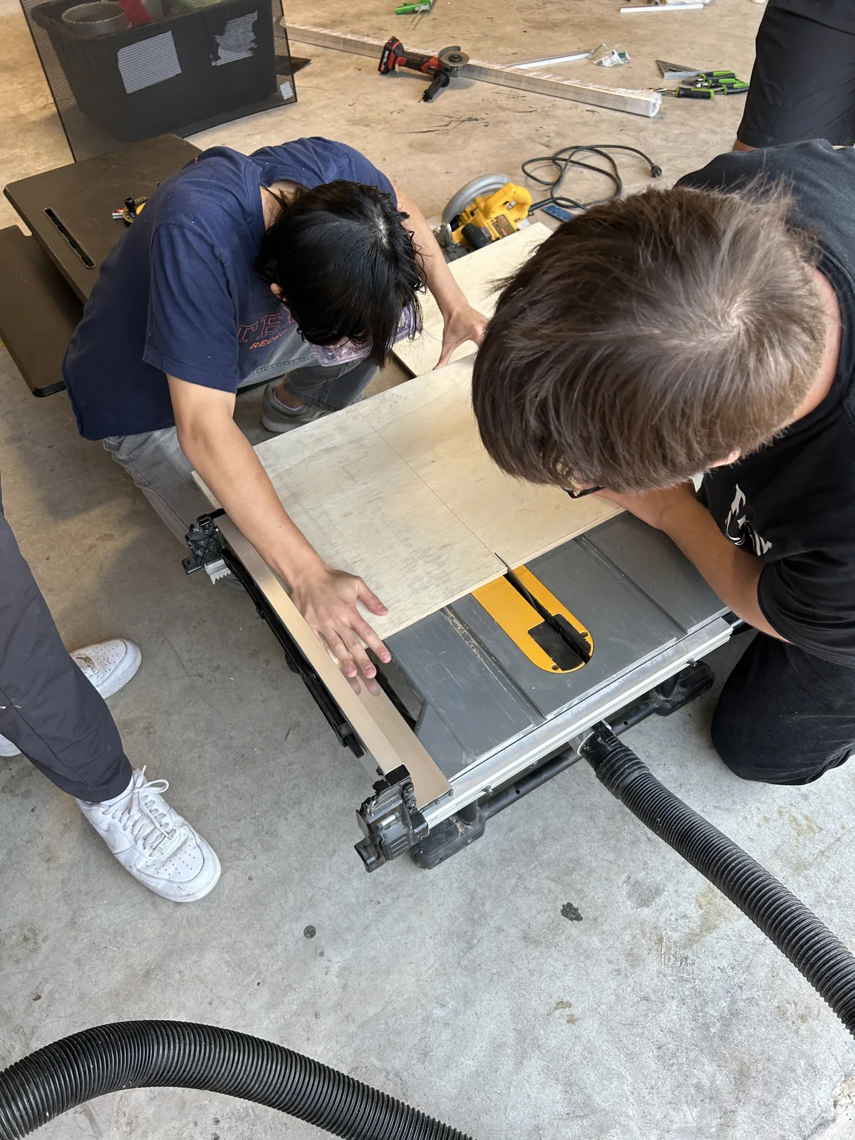 Overhead view of two students guiding a wide board through a table saw together